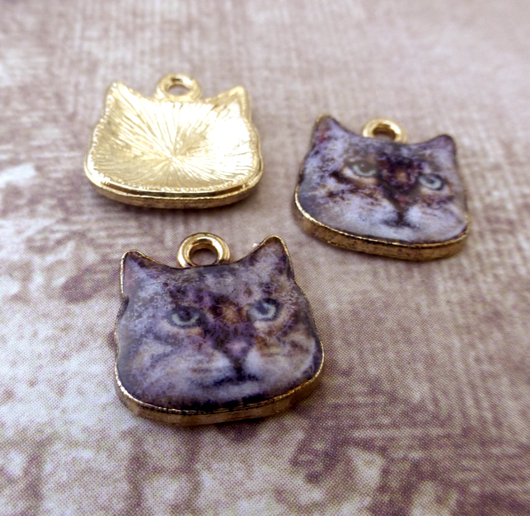 Three cat-shaped charms on a textured fabric background