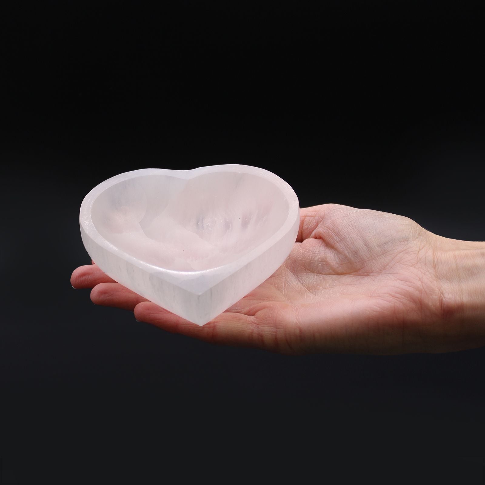 Heart-shaped crystal held in a hand against a black background