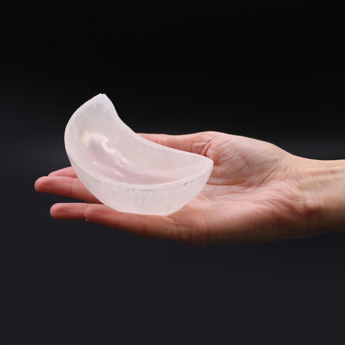 Clear silicone breast implant held in a hand against a black background