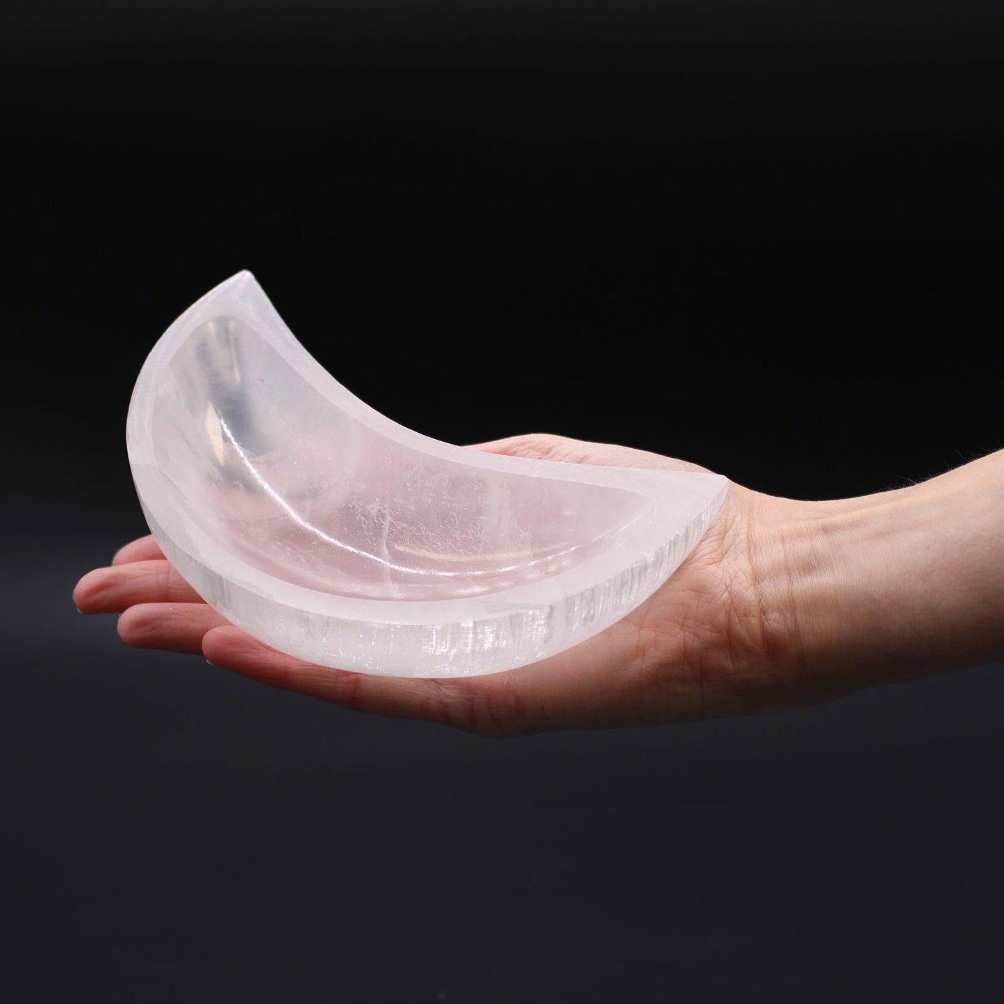 Clear silicone mold shaped like a crescent moon held in a hand against a black background