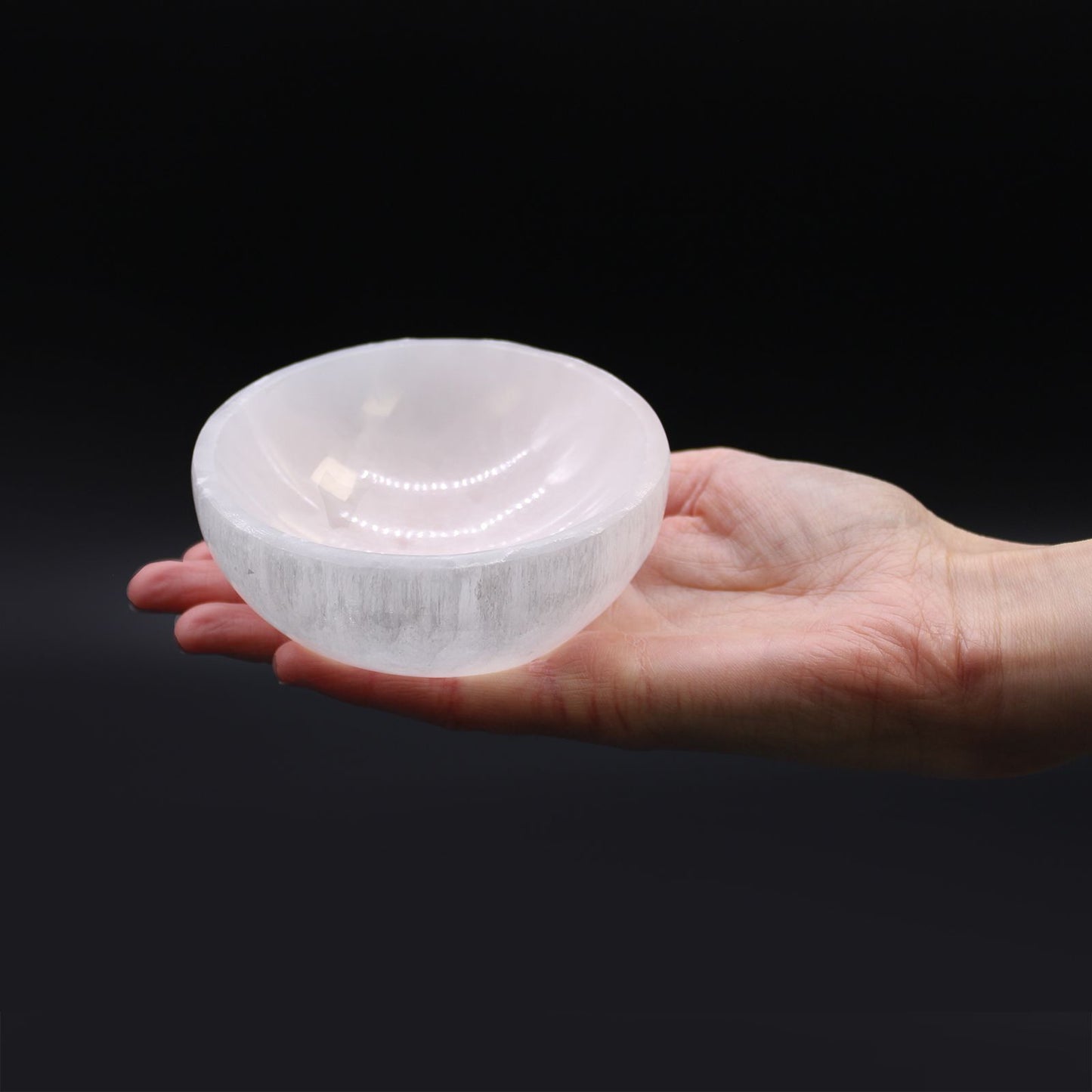 Hand holding a translucent crystal bowl against a black background