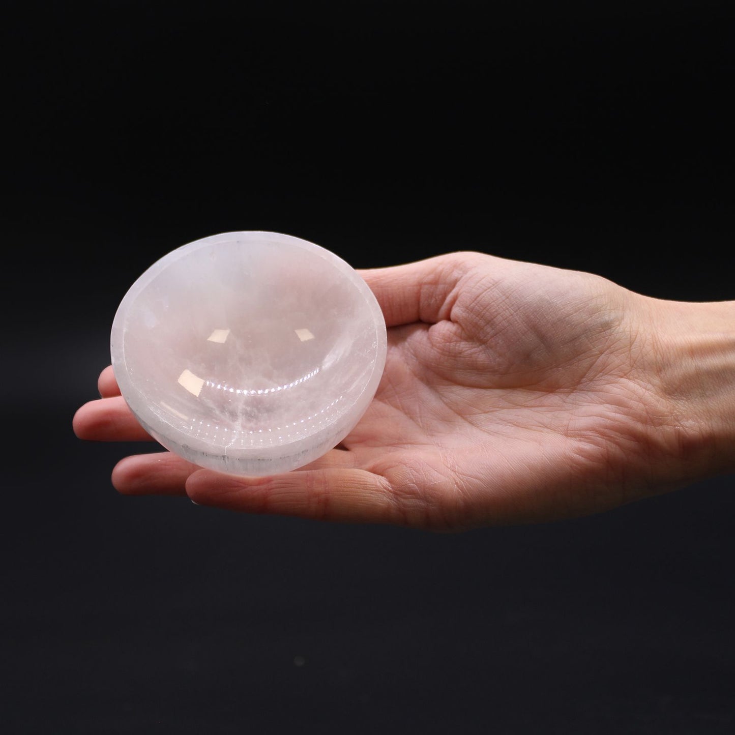 Hand holding a clear crystal ball against a black background
